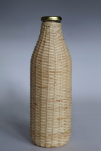 Load image into Gallery viewer, A woven natural fiber bottle cover or decorative bottle wrap with a gold metal cap, shown against a plain gray studio background.
